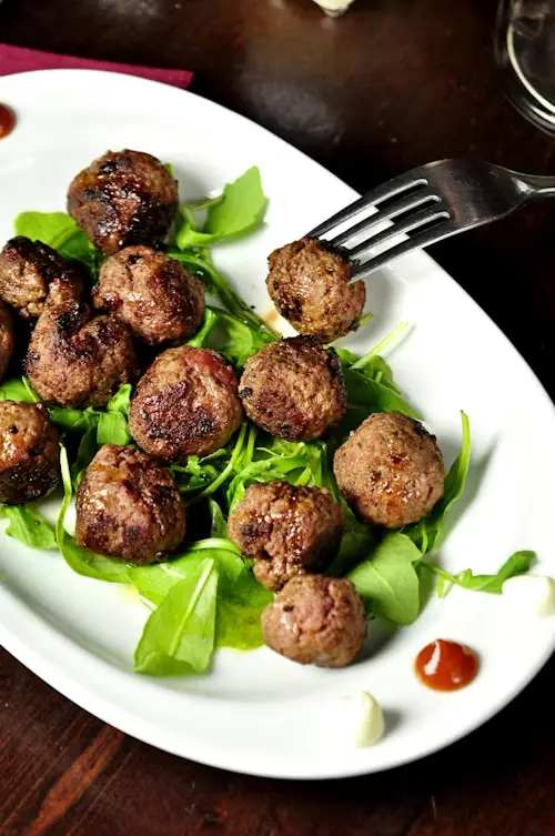 A plate of grilled meatballs served on a bed of fresh greens with dips on the side